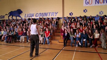 Movie still from “Mean Girls” (2004), directed by Mark Waters – A group of people sitting in front of an audience in a gym; Wide shot, High angle