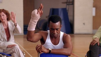 Movie still from “Mean Girls” (2004), directed by Mark Waters – A man with a bandaged arm sits in a gym; Medium shot, Low angle