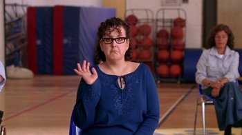 Movie still from “Mean Girls” (2004), directed by Mark Waters – A woman in a blue shirt is sitting in front of a rack of basketballs; Medium shot, High angle