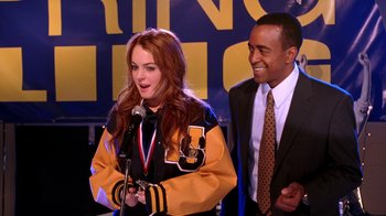 Movie still from “Mean Girls” (2004), directed by Mark Waters – A woman standing next to a man holding a microphone; Medium shot, Over the shoulder angle