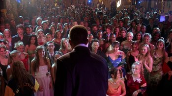 Movie still from “Mean Girls” (2004), directed by Mark Waters – A crowd of people in formal wear standing in front of a man; Wide shot, High angle