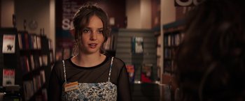 Movie still from “Fear Street: Part One - 1994” (2021), directed by Leigh Janiak – A woman in a floral dress standing in a library; Close Up shot, Over the shoulder angle