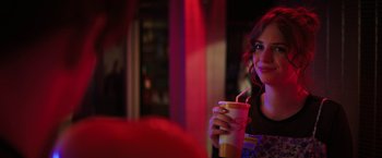 Movie still from “Fear Street: Part One - 1994” (2021), directed by Leigh Janiak – A woman holding a drink and smiling for the camera; Close Up shot, Over the shoulder angle