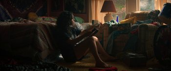 Movie still from “Fear Street: Part One - 1994” (2021), directed by Leigh Janiak – A woman sitting on the floor in a living room; Medium shot, High angle