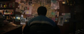 Movie still from “Fear Street: Part One - 1994” (2021), directed by Leigh Janiak – A man sitting in front of a wall covered with papers; Medium shot, Over the shoulder angle