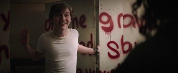 Movie still from “Fear Street: Part One - 1994” (2021), directed by Leigh Janiak – A young man standing in front of a wall covered in graffiti; Medium shot, Over the shoulder angle