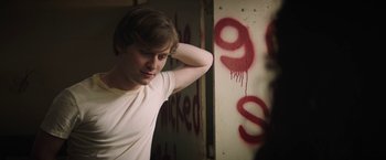 Movie still from “Fear Street: Part One - 1994” (2021), directed by Leigh Janiak – A young man standing in front of a wall covered in graffiti; Medium shot, Over the shoulder angle