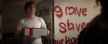 Movie still from “Fear Street: Part One - 1994” (2021), directed by Leigh Janiak – A person holding a box in front of a wall with graffiti; Medium shot, Over the shoulder angle