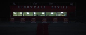 Movie still from “Fear Street: Part One - 1994” (2021), directed by Leigh Janiak – A red and white stadium at night time; Extreme Wide shot, High angle