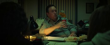 Movie still from “Fear Street: Part One - 1994” (2021), directed by Leigh Janiak – A man sitting at a table holding a cell phone; Medium shot, Low angle