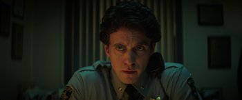 Movie still from “Fear Street: Part One - 1994” (2021), directed by Leigh Janiak – A man in a police uniform is sitting at a desk; Close Up shot, Low angle