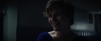 Movie still from “Fear Street: Part One - 1994” (2021), directed by Leigh Janiak – A young woman smiles brightly in a dark room; Close Up shot, Over the shoulder angle