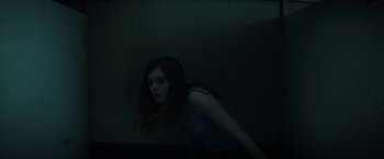 Movie still from “Fear Street: Part One - 1994” (2021), directed by Leigh Janiak – A woman standing in a dark room with her head turned to the side; Medium shot, High angle