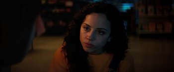 Movie still from “Fear Street: Part One - 1994” (2021), directed by Leigh Janiak – A woman with long curly black hair wearing an orange shirt; Close Up shot, Over the shoulder angle