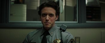 Movie still from “Fear Street: Part One - 1994” (2021), directed by Leigh Janiak – A man in a police uniform is holding a microphone; Close Up shot, Low angle