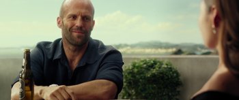 Movie still from “Mechanic: Resurrection” (2016), directed by Dennis Gansel – A bald man sitting in front of some bushes and trees; Close Up shot, Over the shoulder angle