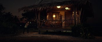 Movie still from “Mechanic: Resurrection” (2016), directed by Dennis Gansel – A wooden hut with a thatched roof at night; Extreme Wide shot, Over the shoulder angle