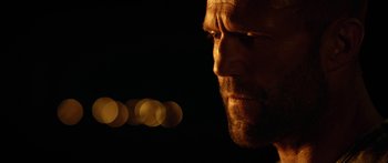 Movie still from “Mechanic: Resurrection” (2016), directed by Dennis Gansel – A person's face with lights in the background; Close Up shot, Over the shoulder angle