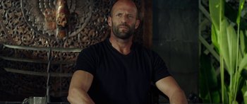 Movie still from “Mechanic: Resurrection” (2016), directed by Dennis Gansel – A bald man with a black t - shirt is looking at the camera; Close Up shot, Over the shoulder angle