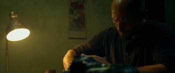 Movie still from “Mechanic: Resurrection” (2016), directed by Dennis Gansel – A man sitting at a table in a dark room; Close Up shot, Low angle