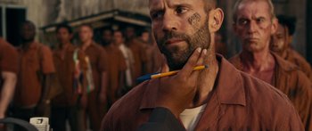 Movie still from “Mechanic: Resurrection” (2016), directed by Dennis Gansel – A man with a beard and a tattoo on his face is holding a pencil in his hand; Close Up shot, Over the shoulder angle