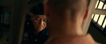 Movie still from “Mechanic: Resurrection” (2016), directed by Dennis Gansel – An older man wearing a hat looking at his reflection in a mirror; Close Up shot, Over the shoulder angle
