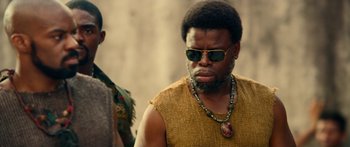 Movie still from “Mechanic: Resurrection” (2016), directed by Dennis Gansel – A man with a beard wearing sunglasses and a necklace; Close Up shot, Low angle