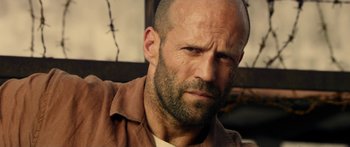 Movie still from “Mechanic: Resurrection” (2016), directed by Dennis Gansel – A man with a beard is looking at the camera; Close Up shot, Low angle