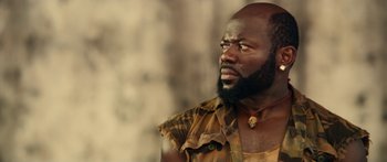 Movie still from “Mechanic: Resurrection” (2016), directed by Dennis Gansel – A man with a black beard and a brown shirt is looking to his left; Close Up shot, Low angle