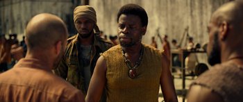 Movie still from “Mechanic: Resurrection” (2016), directed by Dennis Gansel – A man in a yellow shirt is standing next to another man in a yellow shirt; Close Up shot, Over the shoulder angle