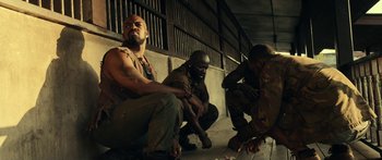 Movie still from “Mechanic: Resurrection” (2016), directed by Dennis Gansel – A group of men sitting next to each other on the ground; Medium shot, Low angle