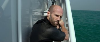 Movie still from “Mechanic: Resurrection” (2016), directed by Dennis Gansel – A man with a shaved head is leaning against a wall; Close Up shot, Low angle