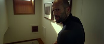 Movie still from “Mechanic: Resurrection” (2016), directed by Dennis Gansel – A bald man in a black wetsuit in front of a wall; Medium shot, Low angle