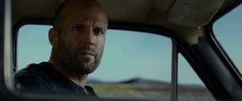 Movie still from “Mechanic: Resurrection” (2016), directed by Dennis Gansel – A man in a car looking out the window; Close Up shot, Over the shoulder angle