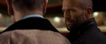 Movie still from “Mechanic: Resurrection” (2016), directed by Dennis Gansel – A person wearing a suit and tie; Close Up shot, Over the shoulder angle