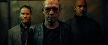 Movie still from “Mechanic: Resurrection” (2016), directed by Dennis Gansel – A man wearing sunglasses standing next to another man; Close Up shot, Low angle