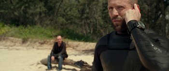 Movie still from “Mechanic: Resurrection” (2016), directed by Dennis Gansel – Two men in wetsuits sitting on the beach; Medium shot, Over the shoulder angle