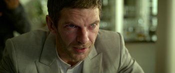 Movie still from “Mechanic: Resurrection” (2016), directed by Dennis Gansel – A person wearing a suit and tie; Close Up shot, Over the shoulder angle