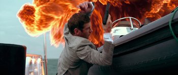 Movie still from “Mechanic: Resurrection” (2016), directed by Dennis Gansel – A man holding onto a boat in front of a fire; Medium shot, Low angle