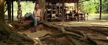 Movie still from “Mechanic: Resurrection” (2016), directed by Dennis Gansel – A woman sitting on the ground in front of a tree; Wide shot, High angle