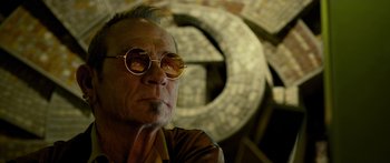 Movie still from “Mechanic: Resurrection” (2016), directed by Dennis Gansel – An older man wearing round glasses looking at the camera; Close Up shot, Low angle