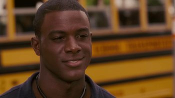 Movie still from “Meet the Browns” (2008), directed by Tyler Perry – A person smiling near a school bus; Close Up shot, Over the shoulder angle