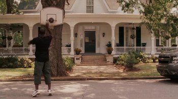 Movie still from “Meet the Browns” (2008), directed by Tyler Perry – A man holding a basketball hoop in front of a house; Wide shot, Low angle