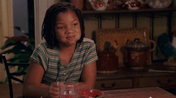Movie still from “Meet the Browns” (2008), directed by Tyler Perry – A girl sitting at a table with a glass of water; Medium shot, Over the shoulder angle