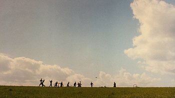 Movie still from “Memphis Belle” (1990), directed by Michael Caton-Jones – A group of people standing on top of a grass covered field; Extreme Wide shot, Low angle