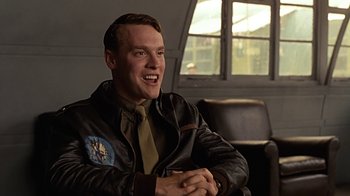Movie still from “Memphis Belle” (1990), directed by Michael Caton-Jones – A man in a leather jacket and a tie sitting in front of a window; Close Up shot, Low angle