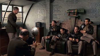 Movie still from “Memphis Belle” (1990), directed by Michael Caton-Jones – A group of men sitting on a chair in a room; Wide shot, High angle