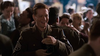 Movie still from “Memphis Belle” (1990), directed by Michael Caton-Jones – A man in a military uniform smiling while holding a cell phone; Close Up shot, Over the shoulder angle