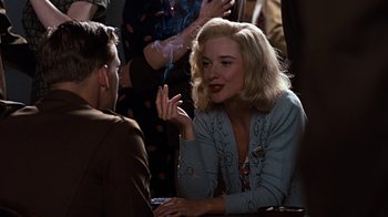 Movie still from “Memphis Belle” (1990), directed by Michael Caton-Jones – A woman sitting at a table talking to a man in front of a crowd; Medium shot, Over the shoulder angle