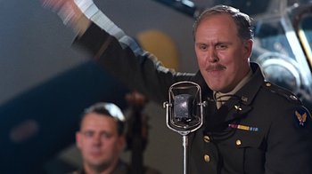 Movie still from “Memphis Belle” (1990), directed by Michael Caton-Jones – A man in a military uniform waves to the crowd; Medium shot, Low angle